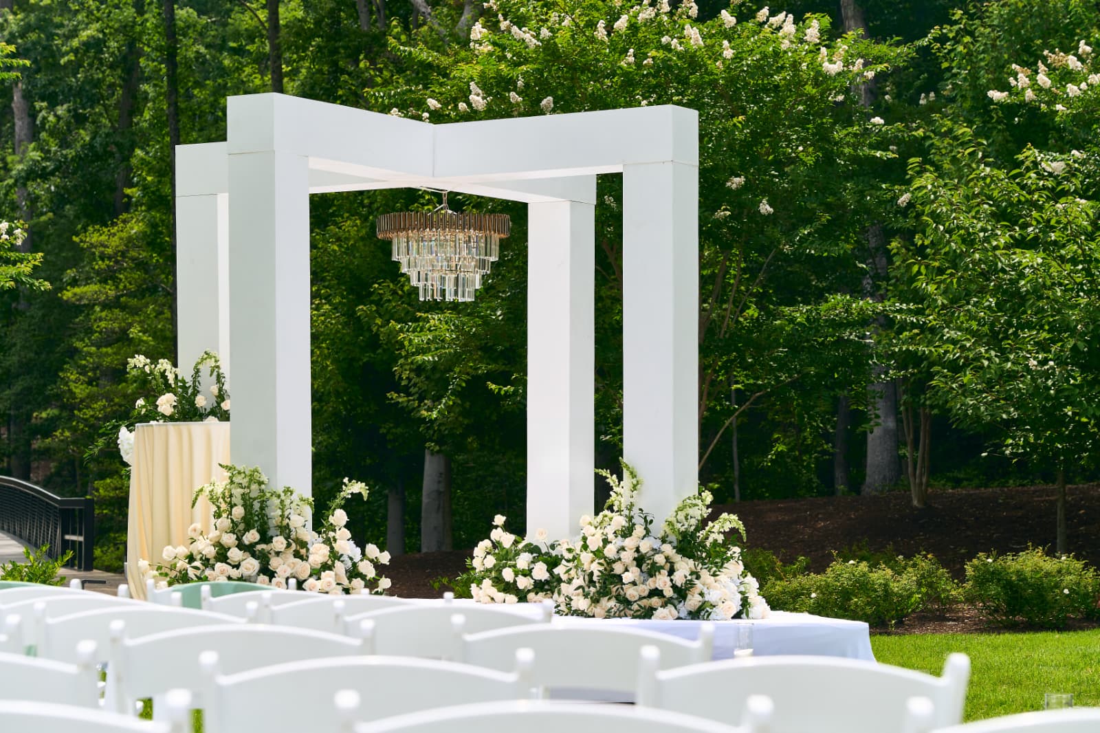 Outdoor wedding ceremony with a white chuppah, chandelier, and white florals